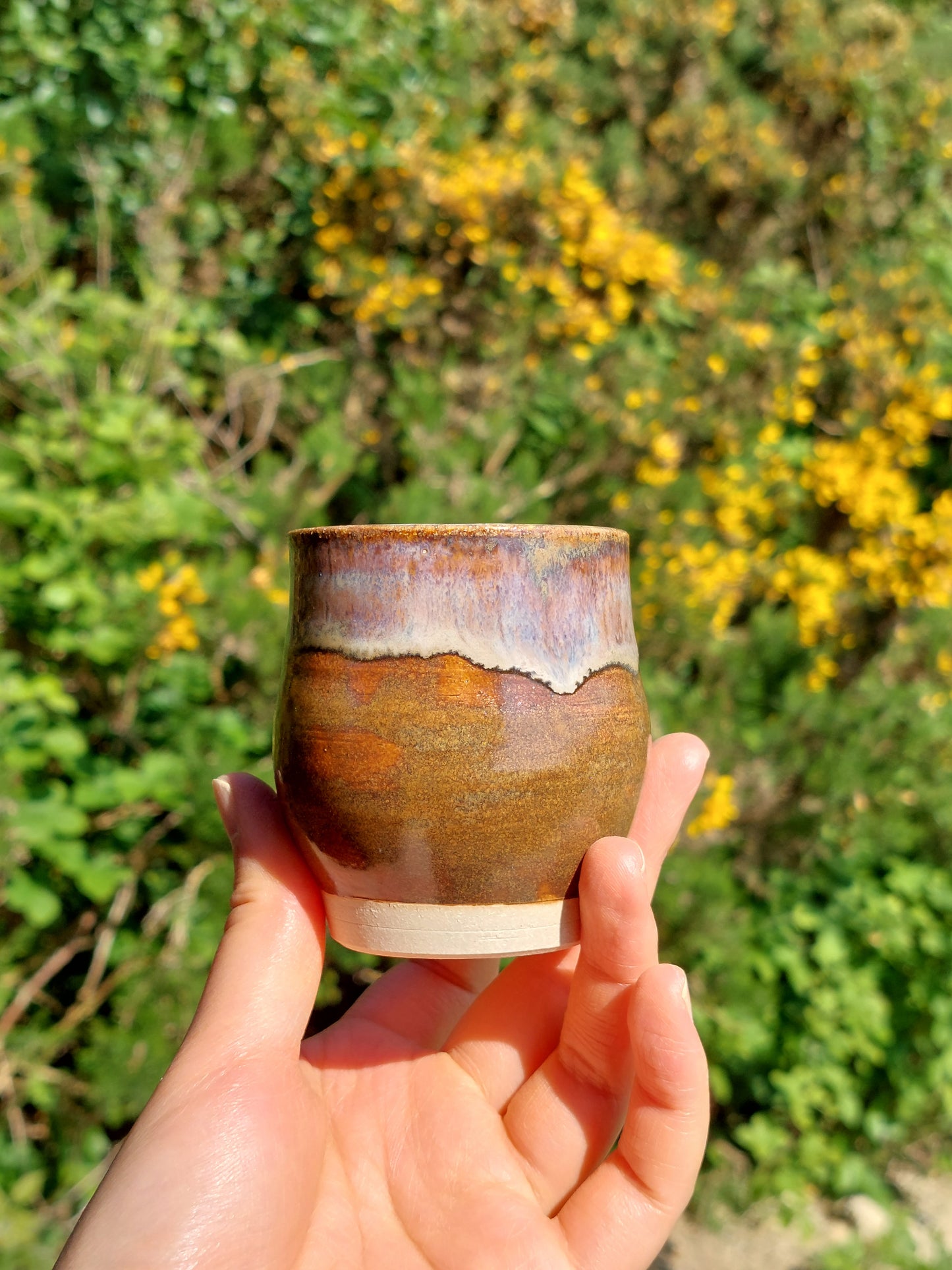 Hand holding a ceramic cup with natural background of greenery and yellow flowers