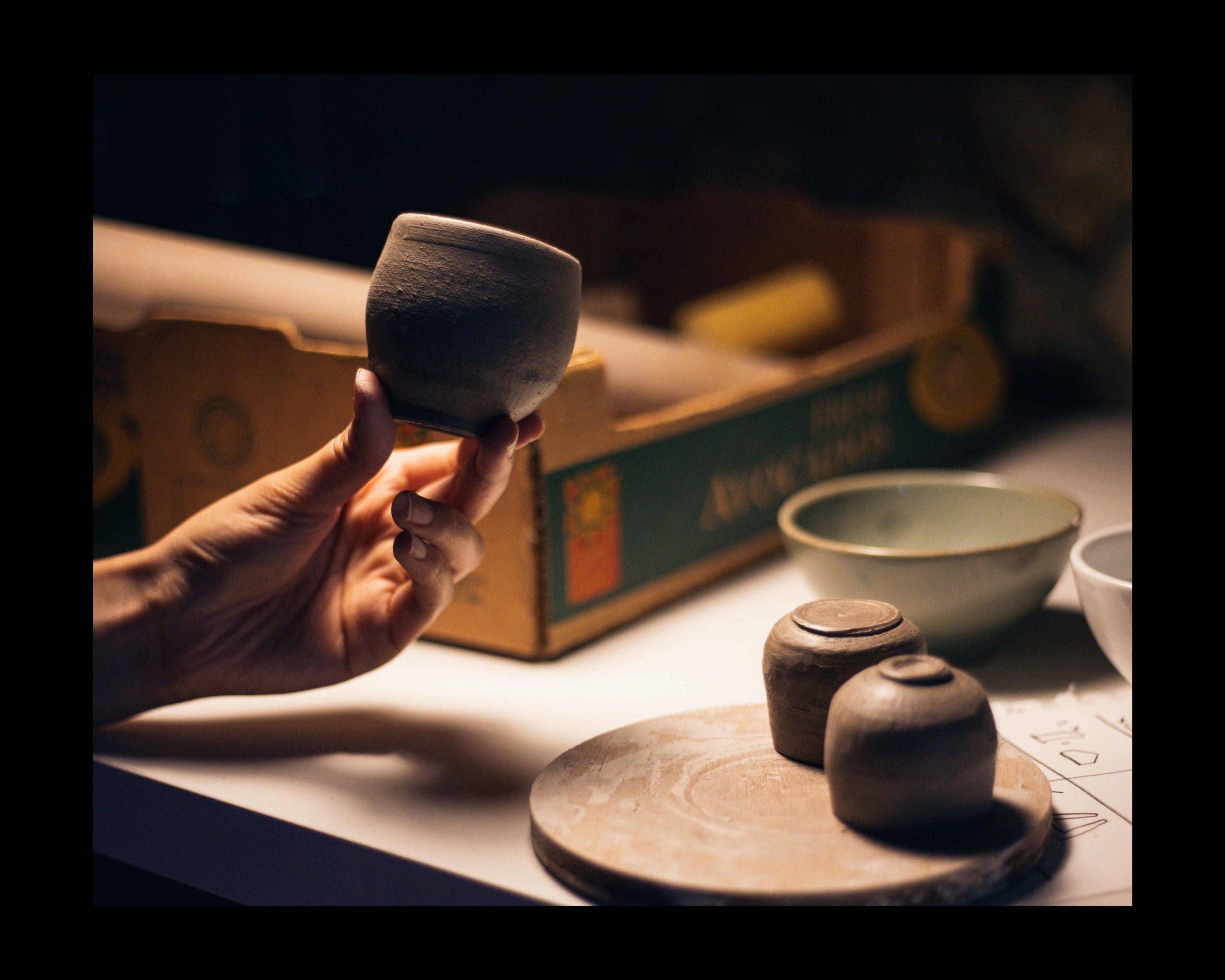 Hand holding a small ceramic cup with more ceramic items on a table.