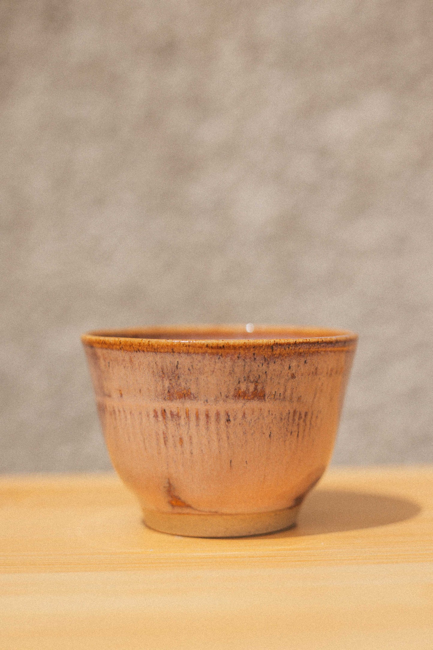 Ceramic cup with brown glaze on a wooden surface and gray background