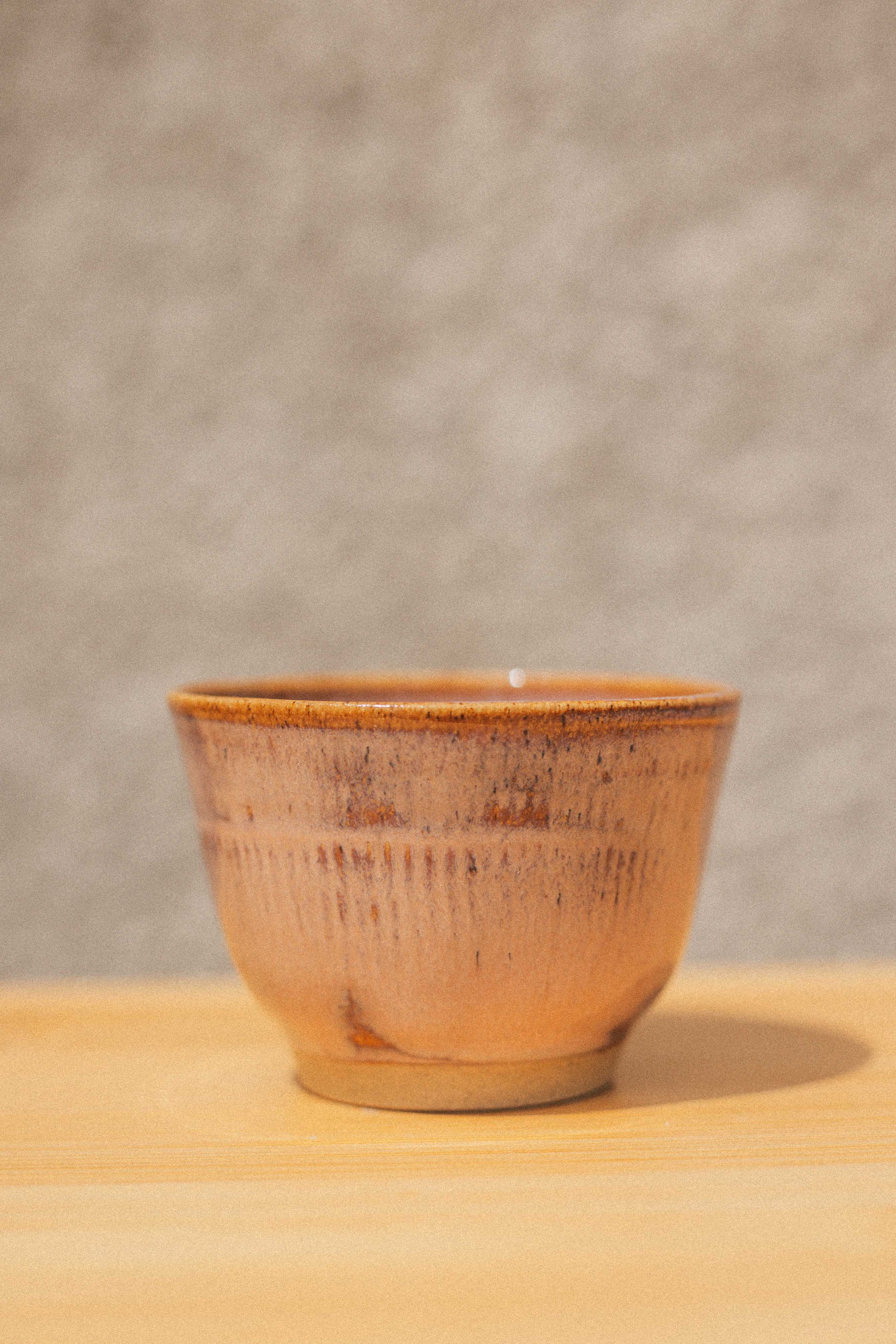 Ceramic cup with brown glaze on a wooden surface and gray background