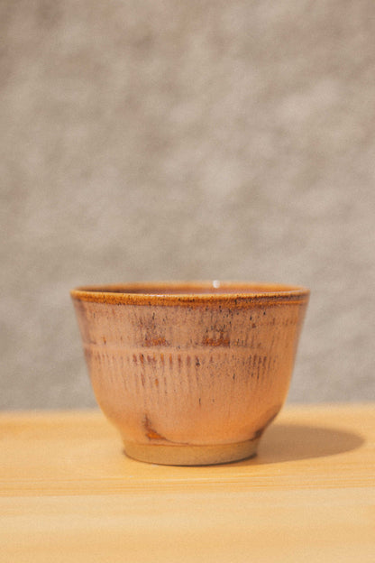 Ceramic cup with brown glaze on a wooden surface and gray background