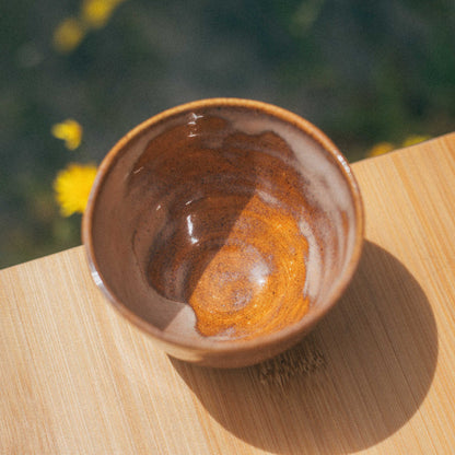 Brown ceramic bowl with orange interior on a wooden surface with blurred greenery in the background