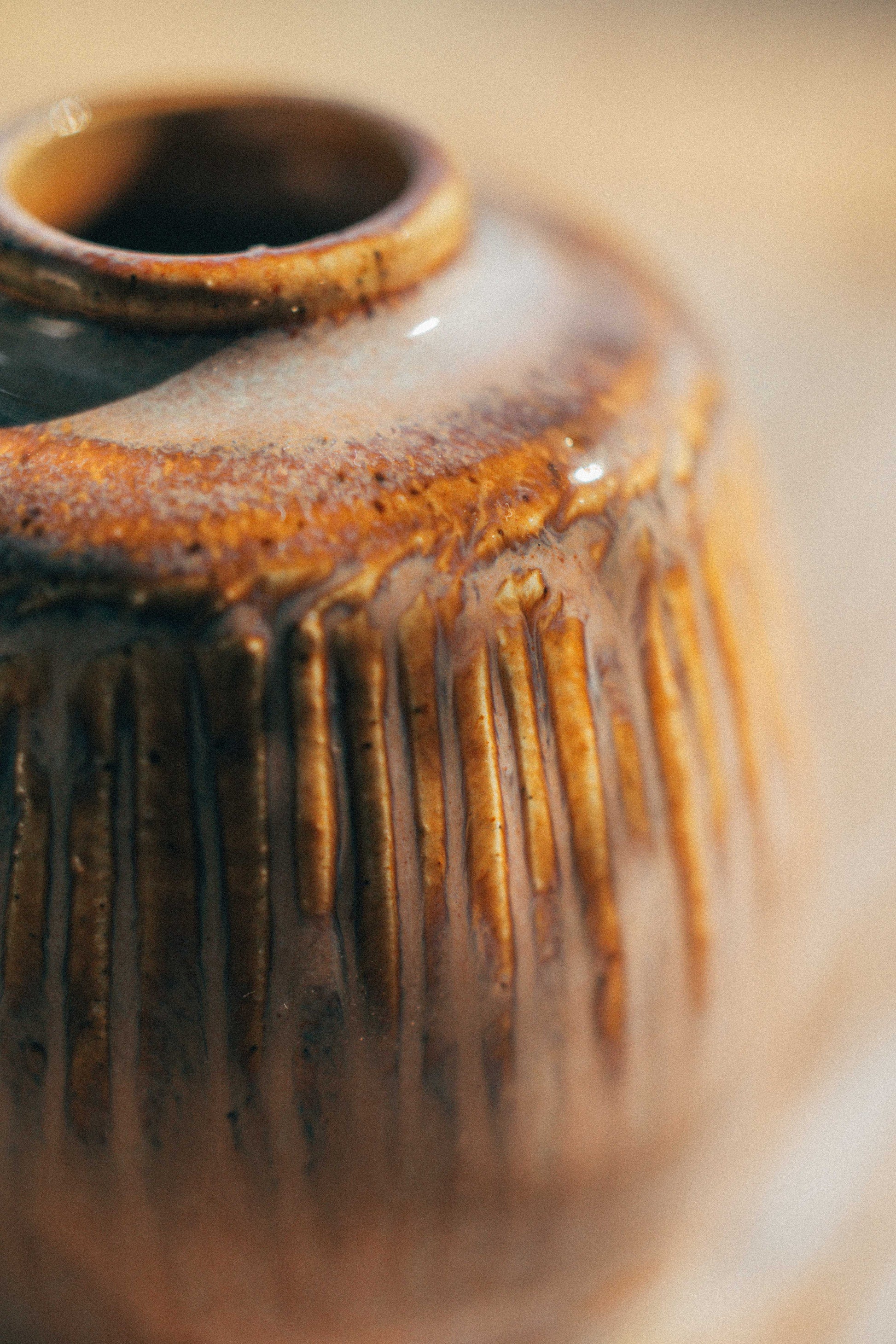 Close-up of a small ceramic vase with a narrow opening, featuring a textured vertical ribbed pattern and a glossy brown and amber glaze.