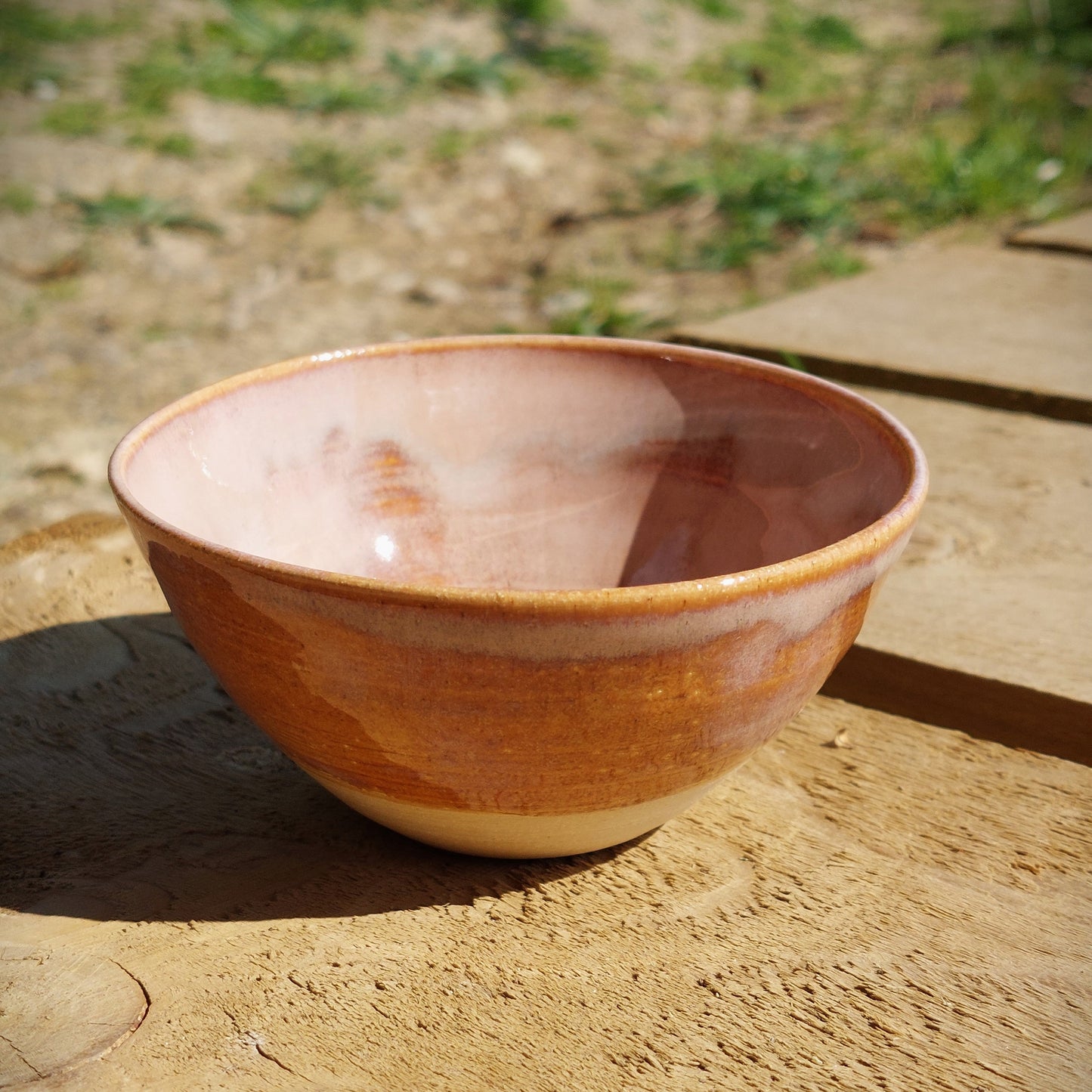 Side view of a bespoke handmade stoneware bowl, glazed in a soft milky pink and breaks golden around the rim of the bowl.