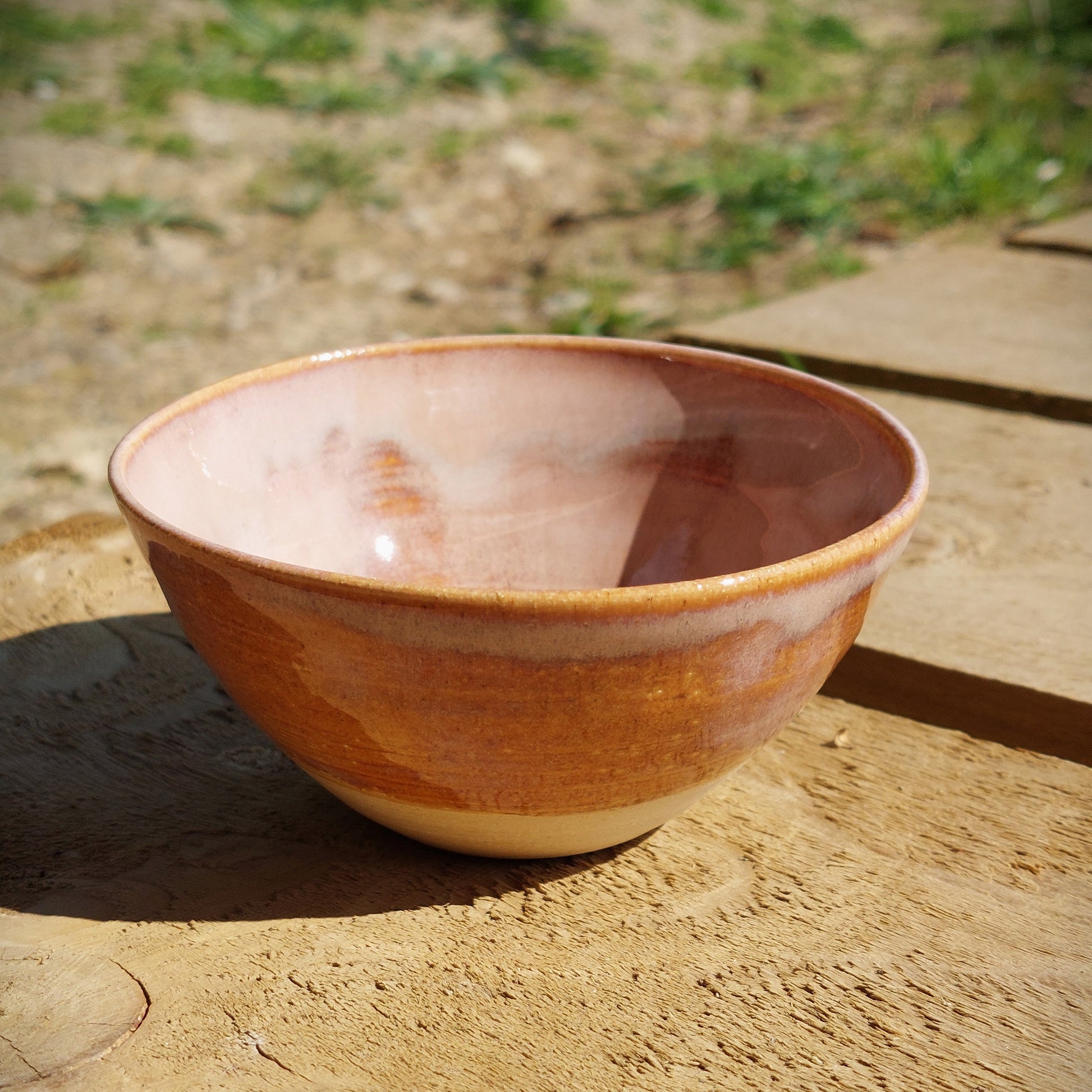 Side view of a bespoke handmade stoneware bowl, glazed in a soft milky pink and breaks golden around the rim of the bowl.